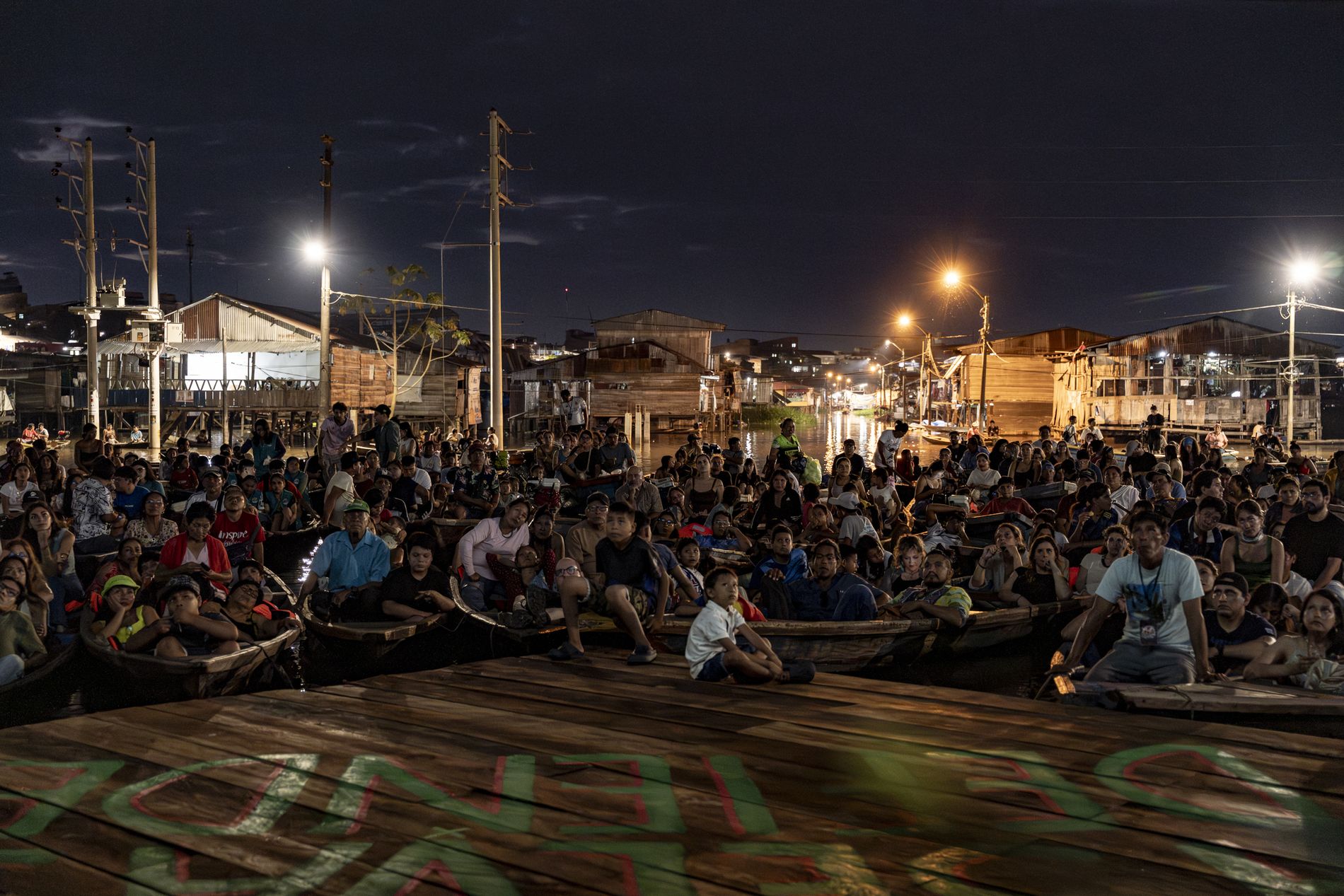 Público reunido en canoas frente a una pantalla durante la noche