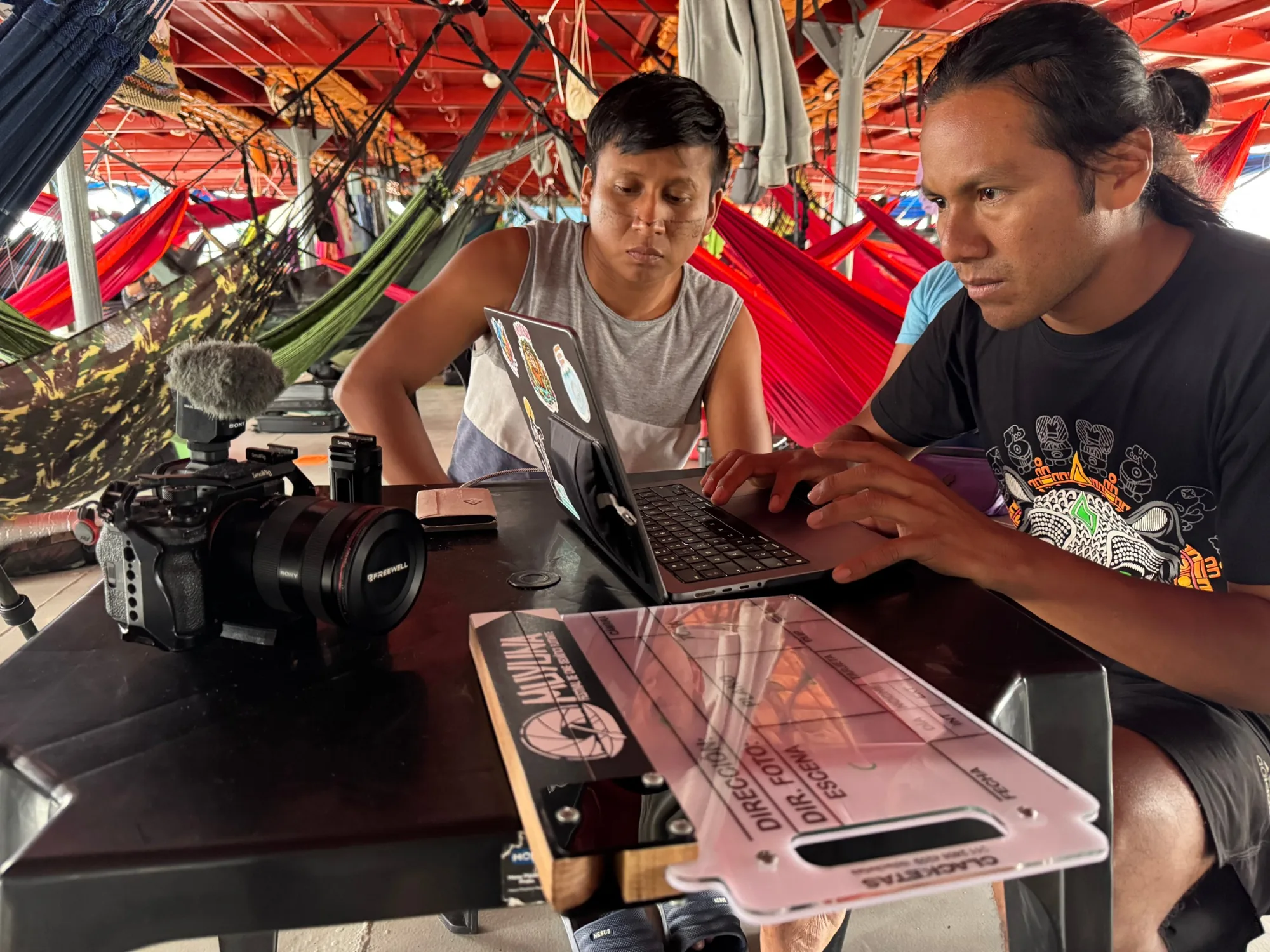 Dos participantes editan en un portátil entre hamacas, a bordo del barco